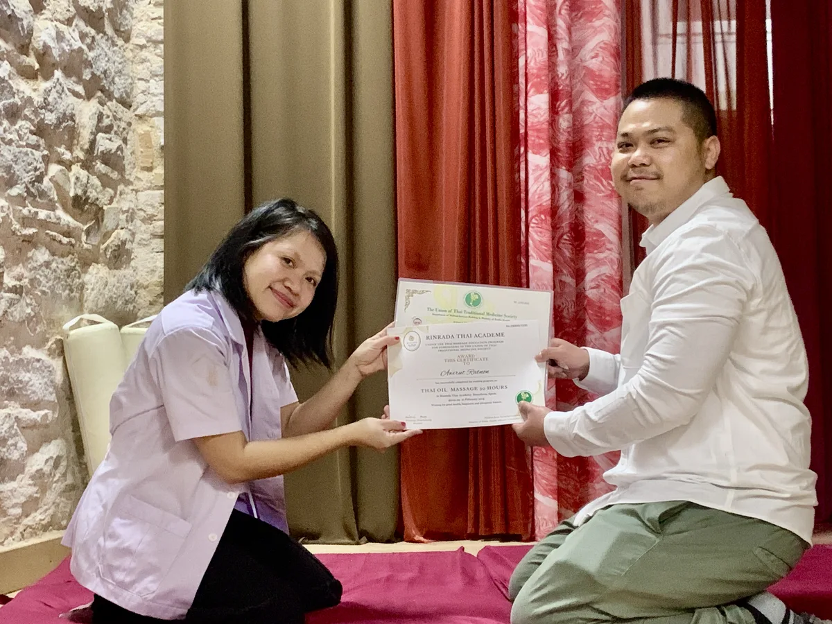 An instructor handing a Union of Thai Traditional Medicine Society certificate to a student