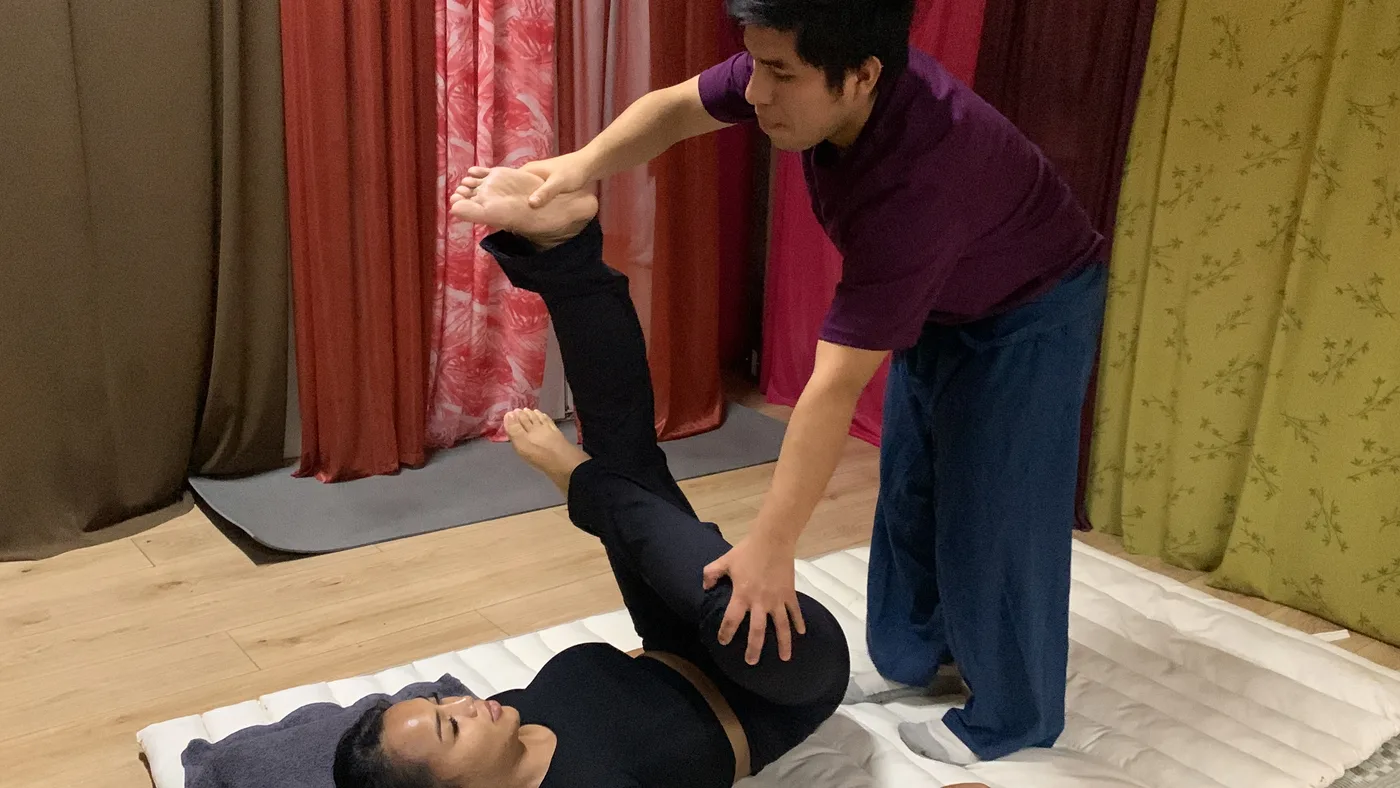 An instructor guiding a student through an assisted stretch on the mat
